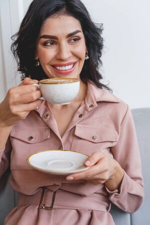 Beautiful young woman holding cup of hot drink and smiling