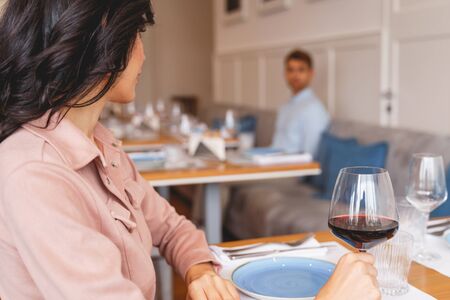 Charming brunette lady holding glass of wine and looking at gentleman in cafeteriaの写真素材