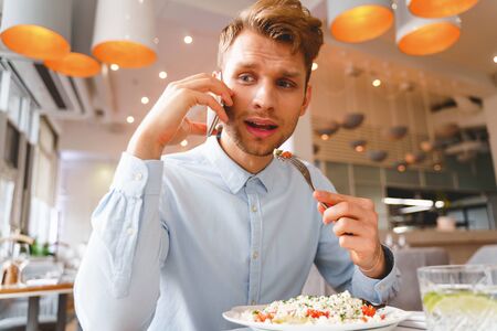 Stylish gentleman talking on mobile phone while eating delicious fresh salad in restaurant