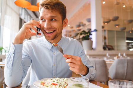 Handsome gentleman talking on mobile phone and smiling while eating delicious salad in restaurantの写真素材