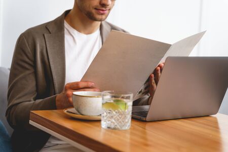 Close up of gentleman choosing food while sitting at cafe table with modern notebook and cup of coffeeの写真素材