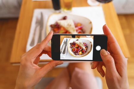 Close up of female hands holding cellphone and photographing fresh salad in cafeの写真素材
