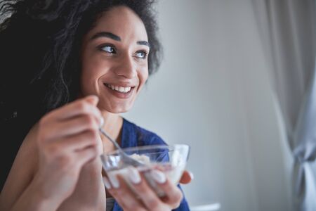 Pretty young woman keeping smile on her face while enjoying her healthy breakfastの写真素材