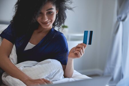 Cute brunette female person keeping smile on her face while enjoying buying clothes in the internet