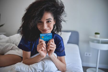 Charming brunette female person holding her debit card while going to buy something onlineの写真素材
