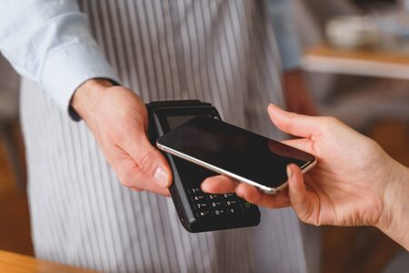 Close up of lady using smartphone to pay for order in restaurant