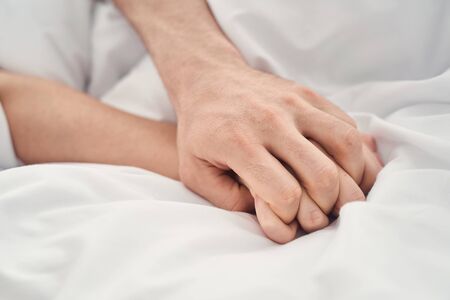 Close up of a Caucasian man and a woman with intertwined fingers making love in bedの写真素材