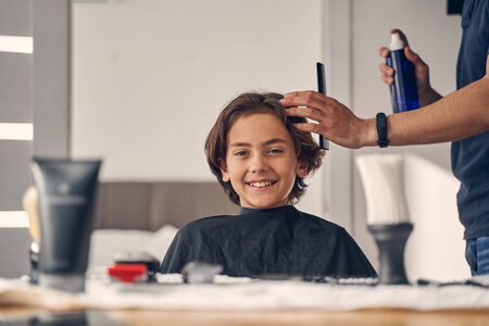 Man in casual clothes changing hairstyle of small kid while using special combの写真素材