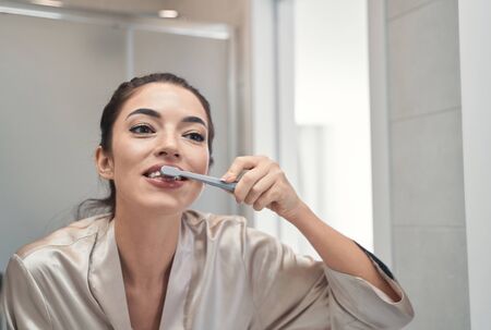 Happy pretty woman with a shiny smile doing morning procedures in a bathroom while brushing teeth with a toothpasteの写真素材