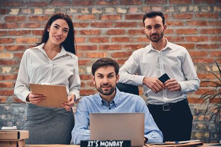 Smiling partners in formal attire holding clipboard and smartphone, working with laptopの写真素材