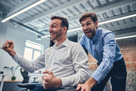 Young smiling male partners having fun in modern office next to workstationの写真素材