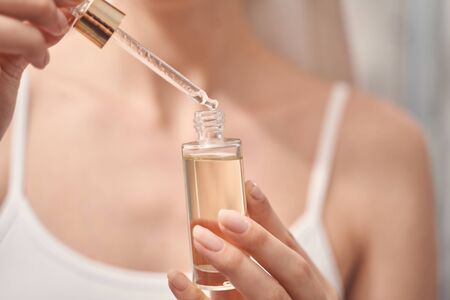 Cropped photo of a Caucasian lady holding a dropper and a bottle of oil in her hands