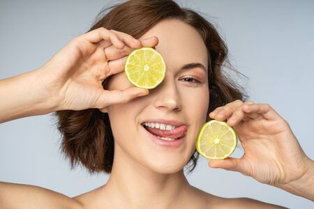 Portrait of smiling pretty female with citrus fruit in hands showing tounge isolated on grey backgroundの写真素材