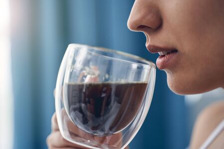 Close up of lady with beautiful plump lips holding glass cup of coffee