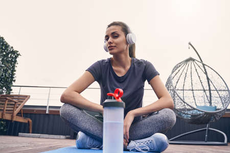 Beautiful sporty lady listening to music through wireless headphones on rooftop terrace