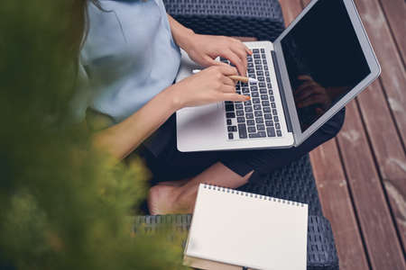 Close up of female hands typing on laptop keyboard while lady sitting in chair with spiral notebookの写真素材