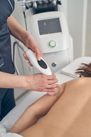 Young woman lying on the medical couch and a cosmetologist using ultrasonic cavitation on her arm...