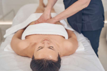 Professional massage therapist touching the belly of a young pretty lad while workingの写真素材