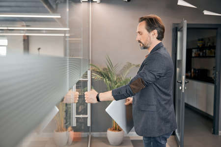 Handsome male holding laptop in his hand and opening the doorの写真素材