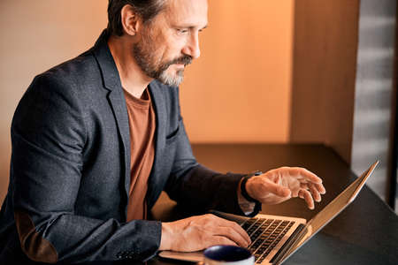 Handsome business executive answering email on laptop inside of the office
