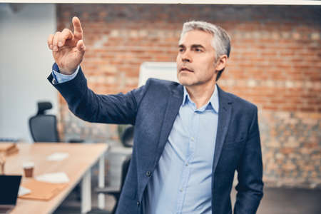 Portrait of seriously mature man holding index finger up and looking at him