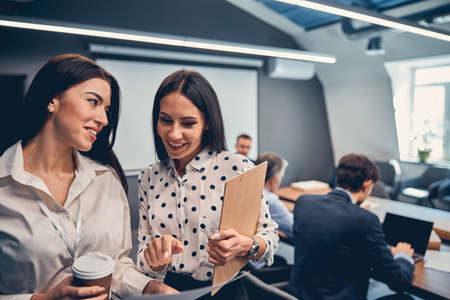 Happy friendly Caucasian businesswoman wearing suit dress talking together in the modern interior officeの写真素材