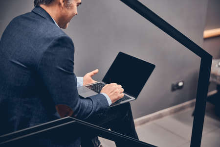Cheerful young businessman holding laptop with black screen while sitting at the office