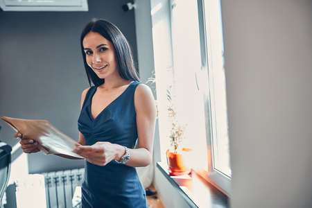 Woman holding clipboard in hand while smiling at the bright workplace