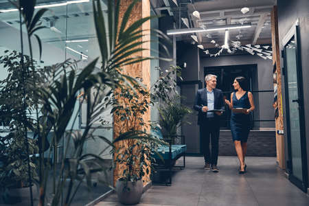 Full length of successful business partners walking along office corridor and speakingの写真素材