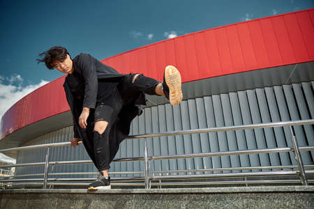 Stylish guy in ripped jeans looking away with serious expression and doing tricks while spending time outdoorsの写真素材