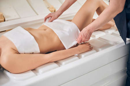 Cropped photo of a young lady lying in a capsule without clothes and hands of beautician putting...