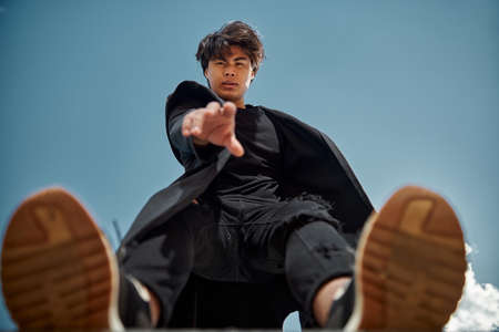 Attractive stylish guy in black outfit reaching out hand and looking at camera with serious expressionの写真素材