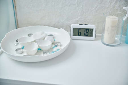 White furniture surface by the wall. Round tray with candles and stones placed near the alarm clock...