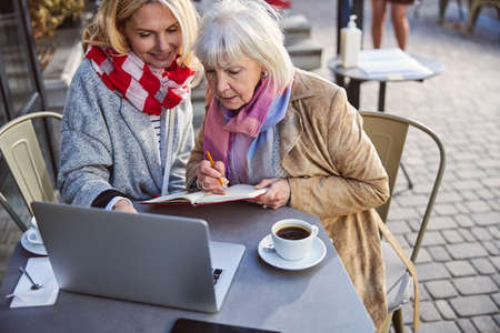 Close up portrait of adult woman teaching another elderly female while using laptop