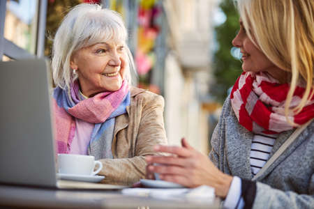 Happy businesswomen talking about something while using laptop outdoors while enjoying coffee