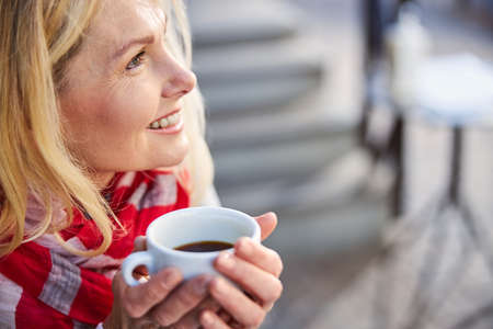 Laughing cheerful woman looking at the sky while holding hot cup of coffee in handの写真素材