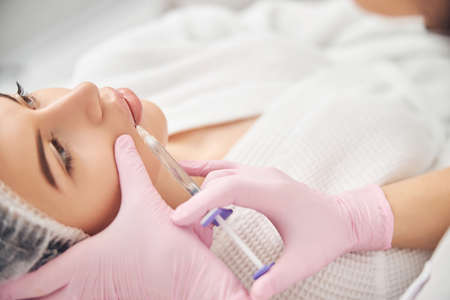 Caucasian female receiving filler injection in lips while resting with open eyesの写真素材