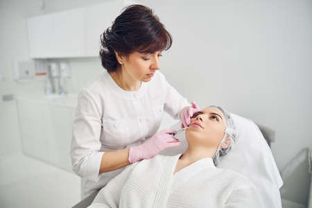 Focused beautician applying medicine in patient lower lip with a syringeの写真素材