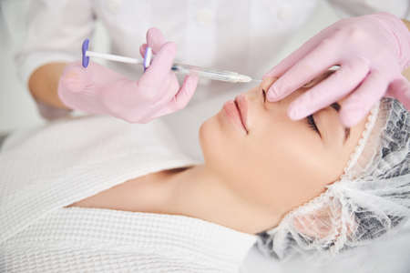 Hands of skillful beauty employee injecting a filler underneath client nose skinの写真素材
