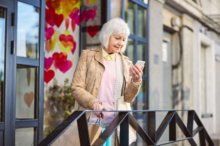 Close up picture of beautiful woman standing near the cafe while looking the screen of smartphone