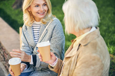 Cheerful lady feeling happy when meeting and talking with her female friend with cup of coffeeの写真素材