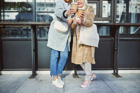 Cropped head of smiling women showing two paper cups of coffee while spending time at the outdoorsの写真素材
