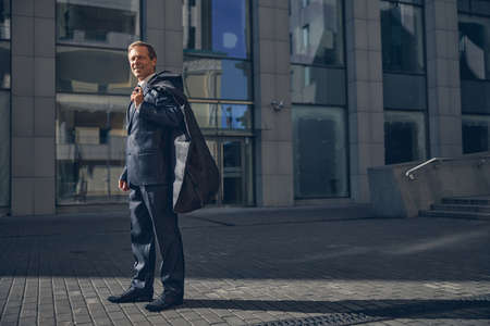 Handsome stylish gentleman looking at camera and smiling while holding suit garment bag