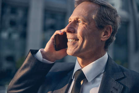 Close up of handsome gentleman in suit having phone conversation and smiling