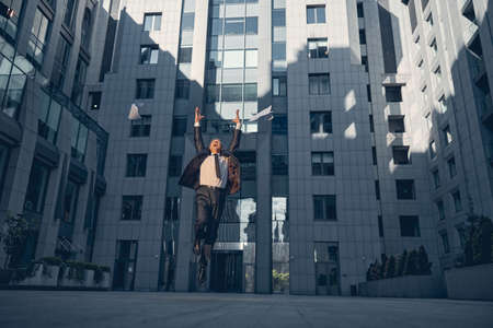 Joyful excited man in elegant suit throwing papers in the air and jumping while celebrating victory...