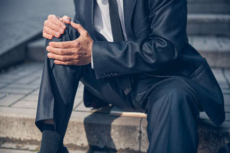 Close up of gentleman sitting on steps and touching his injured knee