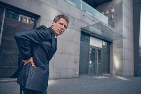 Middle-aged gentleman in suit suffering from backache while spending time outdoors