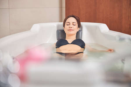 Beautiful serene relaxed young Caucasian lady with her eyes closed lying in the hydromassage bathtub