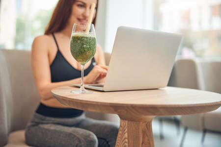 Smiling sporty female typing on her laptop placed on a table in a wellness centerの写真素材