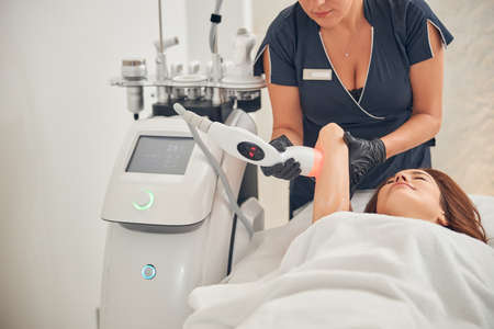 Beautician doing cavitation procedure on arms of a female client at a beauty center while woman...